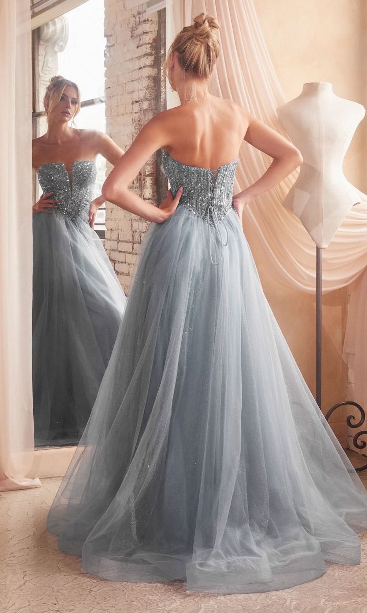 A woman wears the Lace-Up Strapless Long Glitter Prom Dress CD0217, admiring its lace-up back in the mirror while a dress form nearby enhances the elegant atmosphere.